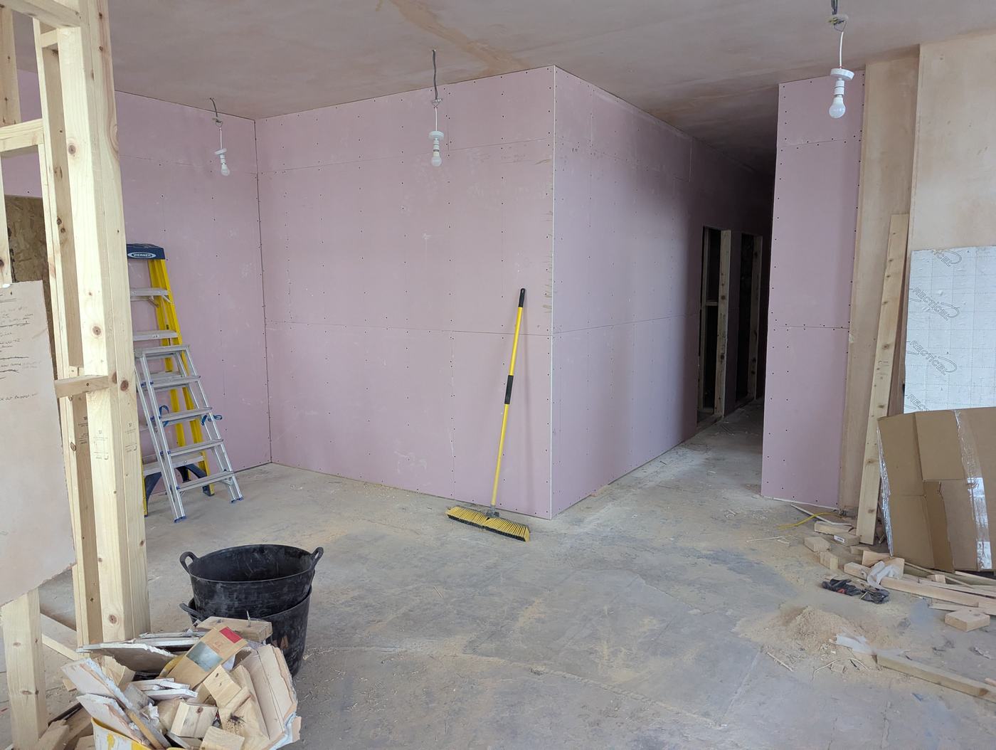 A framed room now fully lined with pink plasterboard on the walls, ready for the finishing coat